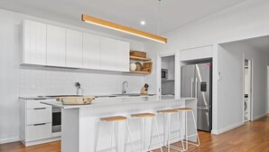 Eine moderne Küche mit weißen Schränken, einer zentralen Kochinsel mit Sitzgelegenheiten, einem eingebauten Backofen und einem Edelstahlkühlschrank.
