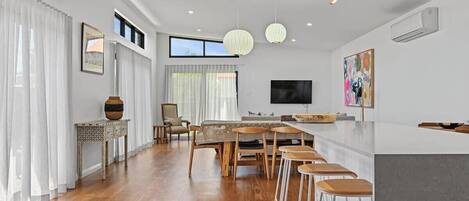 Une cuisine moderne avec un coin repas, un plancher en bois, des luminaires suspendus et une grande fenêtre.