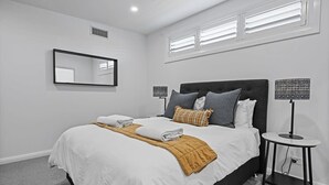 Ein Schlafzimmer mit einem Bett, zwei Nachttischen, einem Spiegel und einem Fenster mit Jalousien.