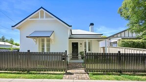 Ein zweistöckiges Haus mit Eingangsbereich, einer kleinen Veranda und einem weißen Zaun.