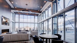 Un hall d’hôtel spacieux, doté d’un grand espace salon, d’une table ronde et de grandes fenêtres offrant une vue sur les montagnes.
