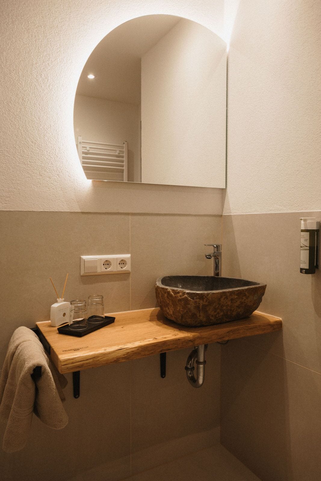 A bathroom with a wooden vanity, a stone sink, a mirror, and a towel hanging on the wall.