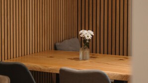 A wooden table with a vase of white flowers, surrounded by two chairs with wooden legs.