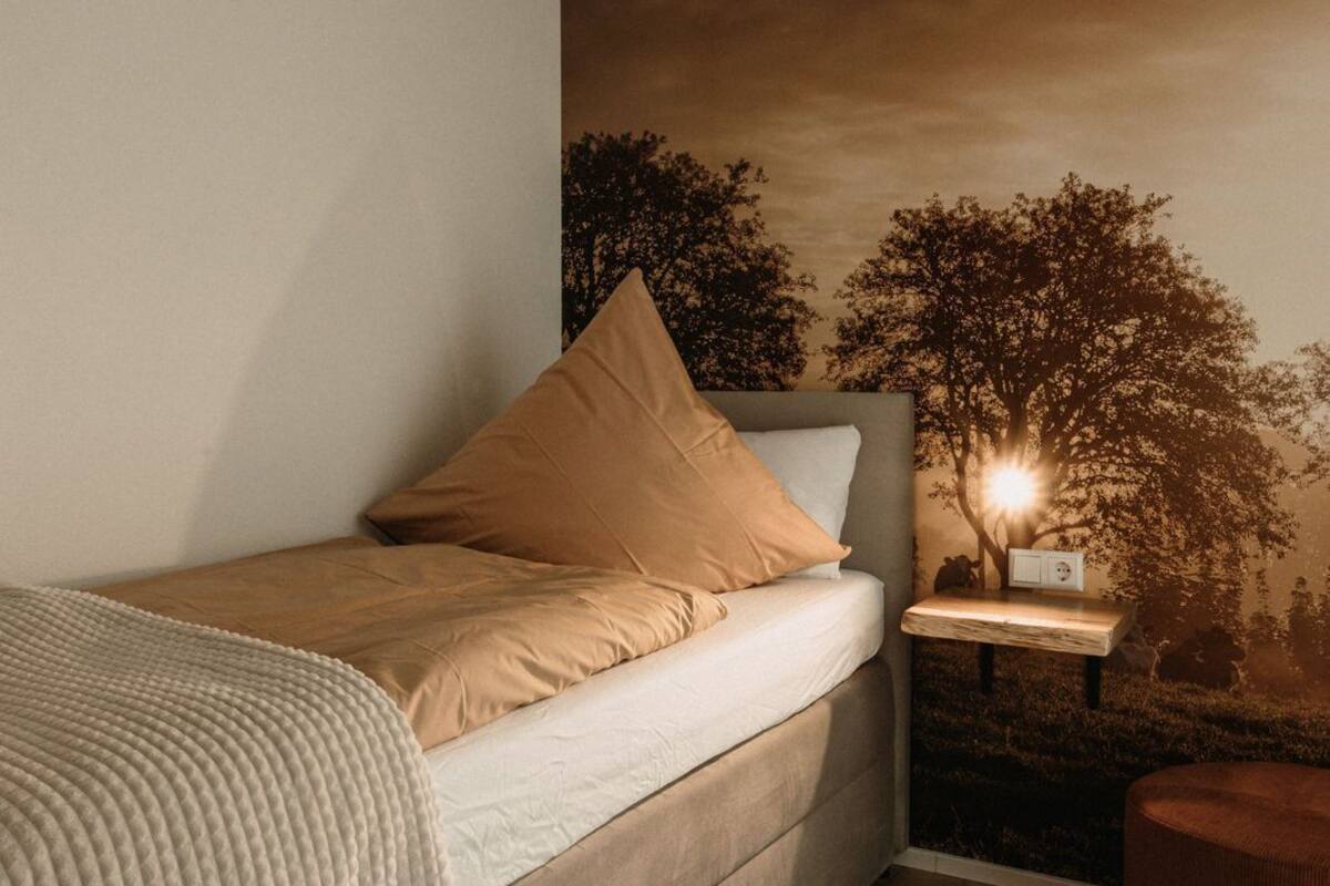 A modern bedroom with a bed, a nightstand, a lamp, and a wall mural.