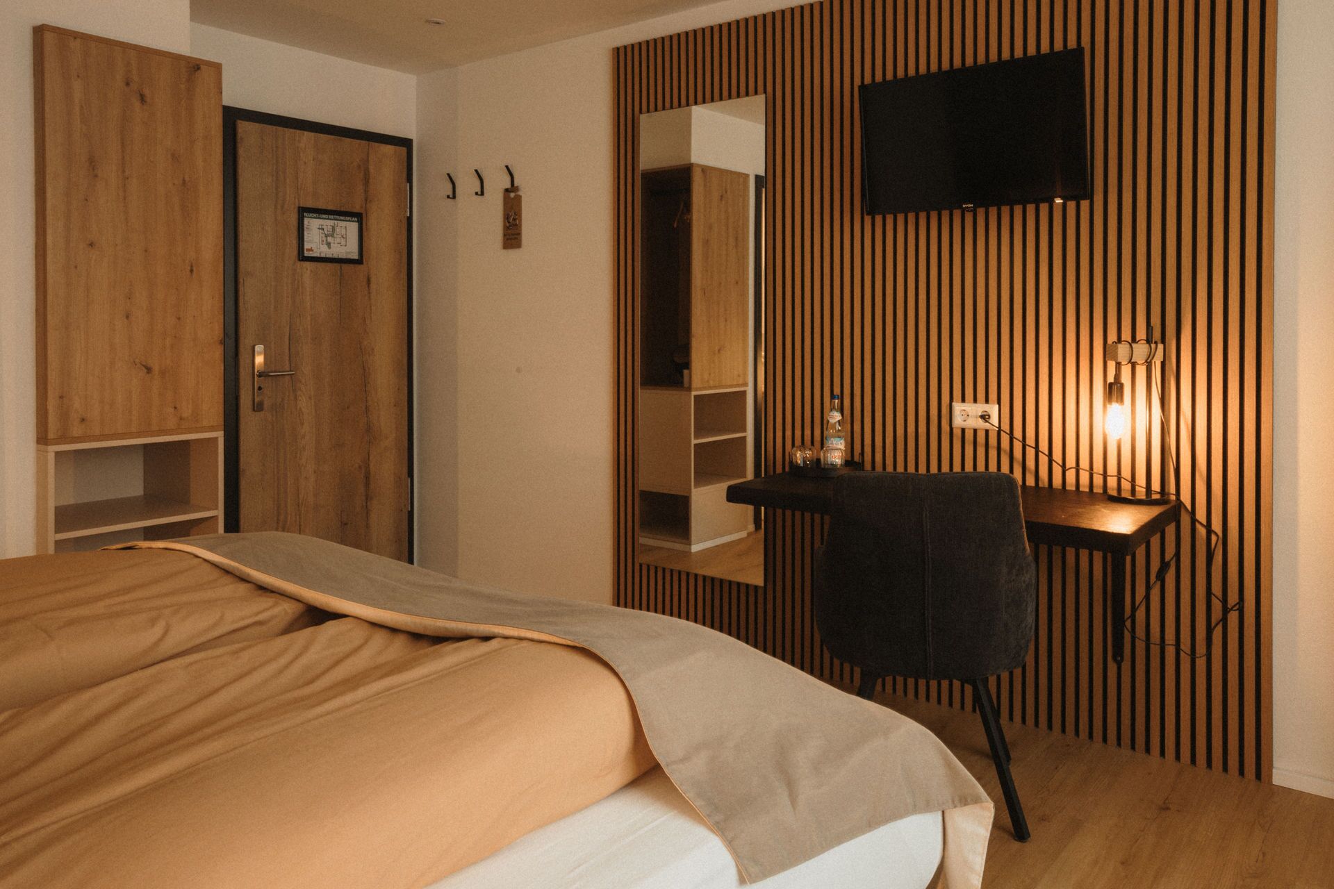 Ein Schlafzimmer mit einem Bett, einem Schreibtisch und einem an einer Holzwand montierten Fernseher.