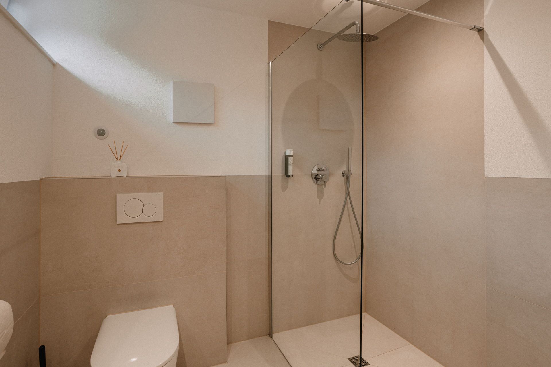 Un baño moderno con cabina de ducha de vidrio, inodoro y difusor de pared.