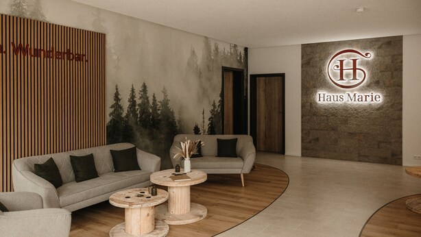 A modern interior with two sofas, round wooden tables, and a logo on the wall.