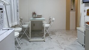 Ein kompaktes, modernes Badezimmer mit weißem Marmorboden, einem kleinen Tisch mit Stühlen, einer Duschkabine mit Vorhängen und einem an der Wand montierten Fernseher.