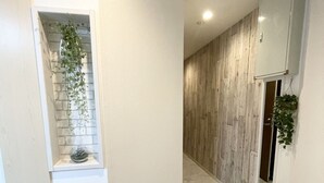 Ein Korridor mit Marmorboden, einer weißen Wand mit einem kleinen Regal, auf dem eine Pflanze steht, und einer Wandpaneelung aus Holz.