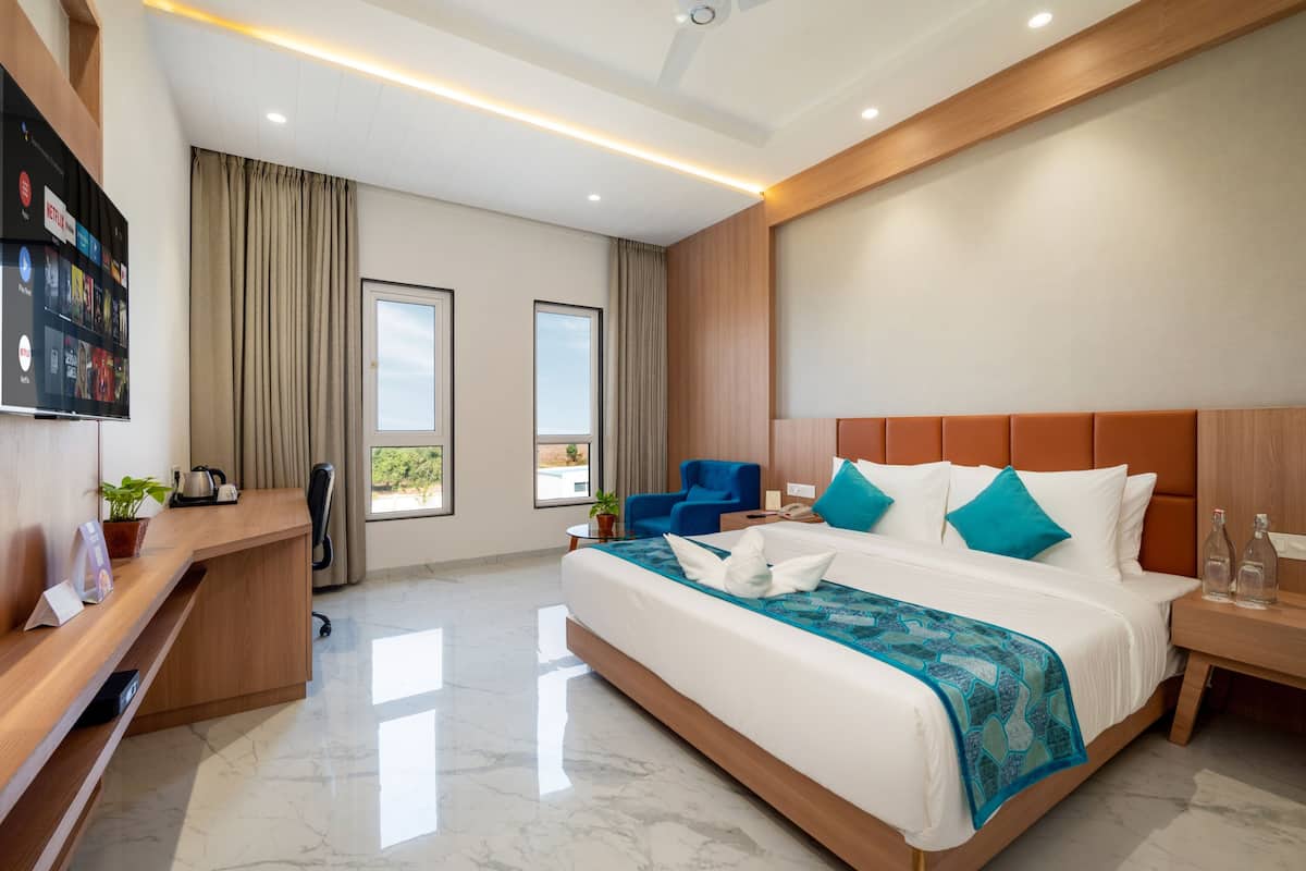 Quarto de hotel moderno com uma cama grande, uma escrivaninha, uma cadeira, uma televisão e vista para o exterior.