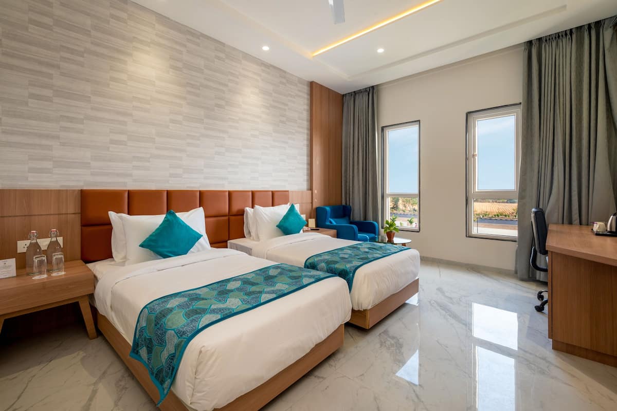 Quarto de hotel moderno com duas camas, cabeceira de madeira, uma escrivaninha e vista para o exterior.