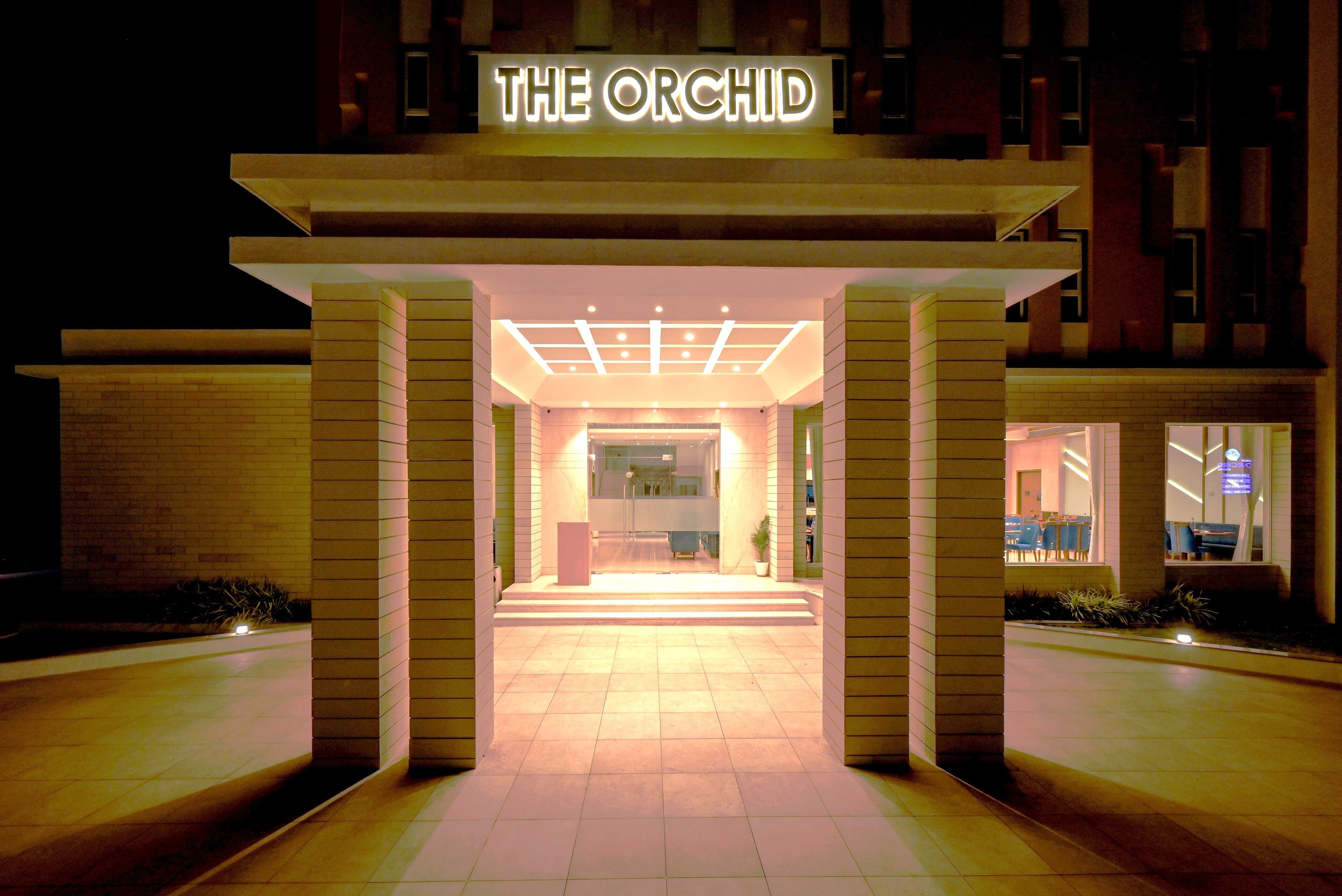 La entrada del hotel Orchid, con un diseño moderno, un letrero iluminado y un interior acogedor.
