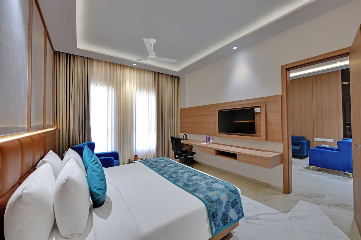 Quarto de hotel com cama, escrivaninha, cadeira, televisão e área de estar com cadeiras.