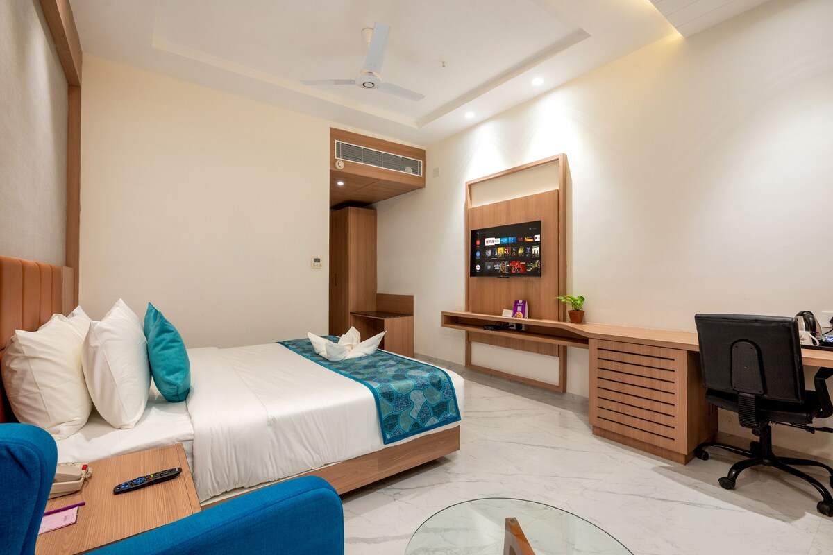 A hotel room with a bed, a desk, a chair, a TV, and a ceiling fan.