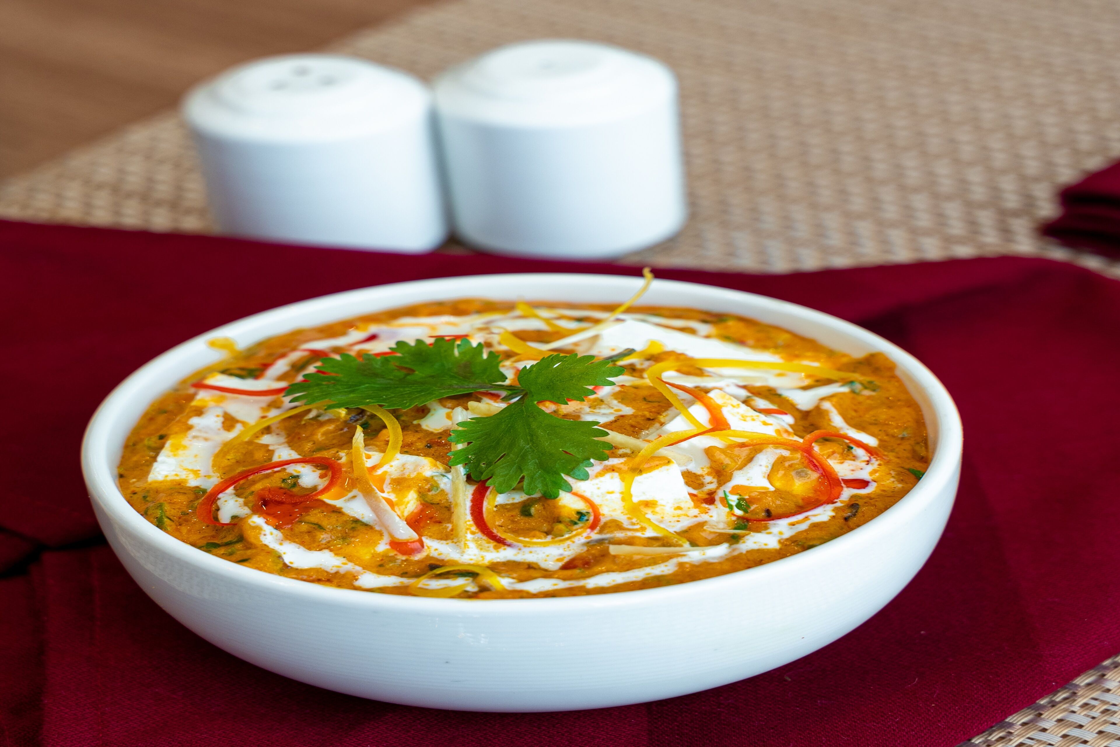 Eine Schüssel Curry mit Garnitur auf einer roten Tischdecke.