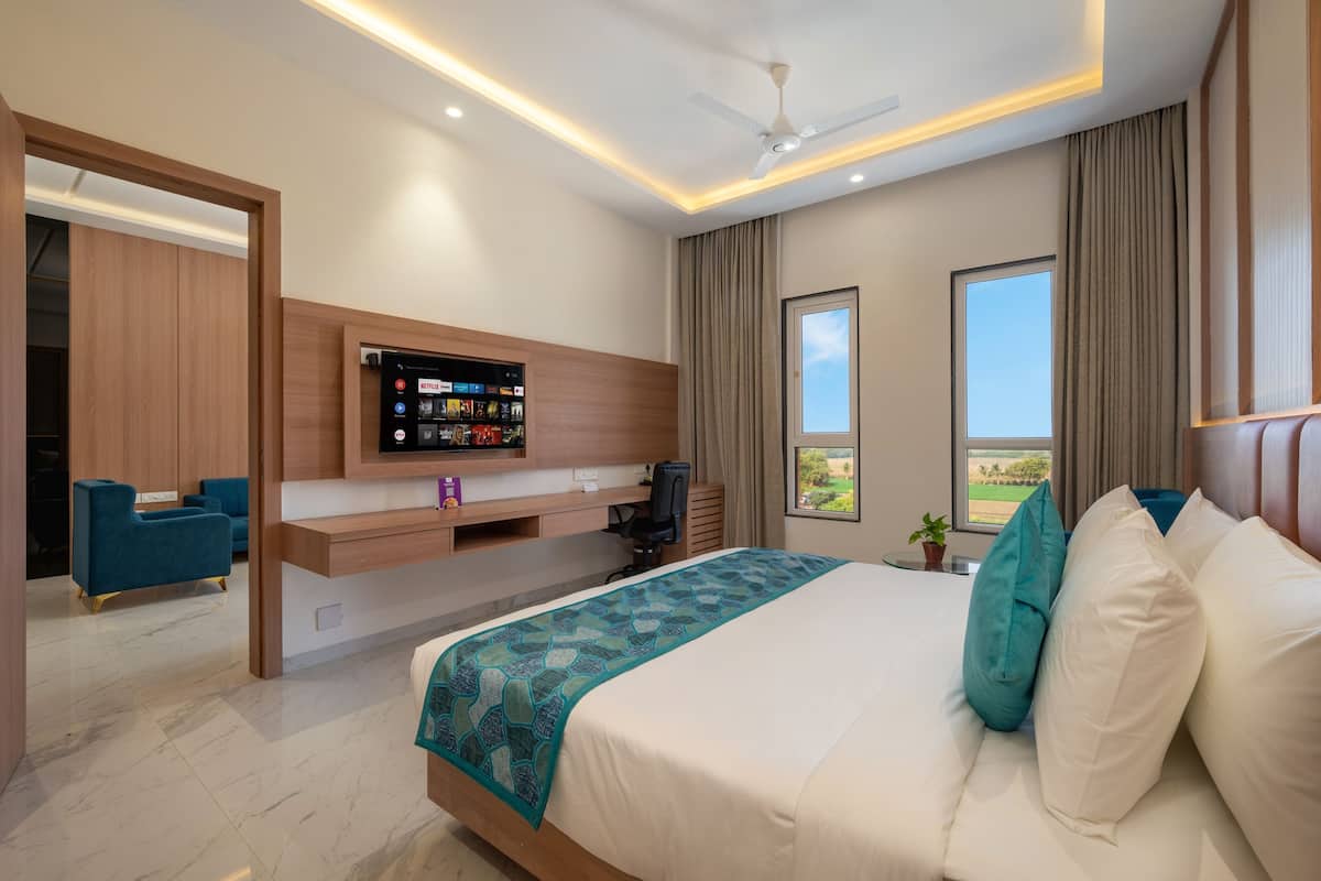 Quarto de hotel moderno com uma cama grande, uma escrivaninha com televisão de tela plana, ventilador de teto e amplas janelas com vista para o exterior.