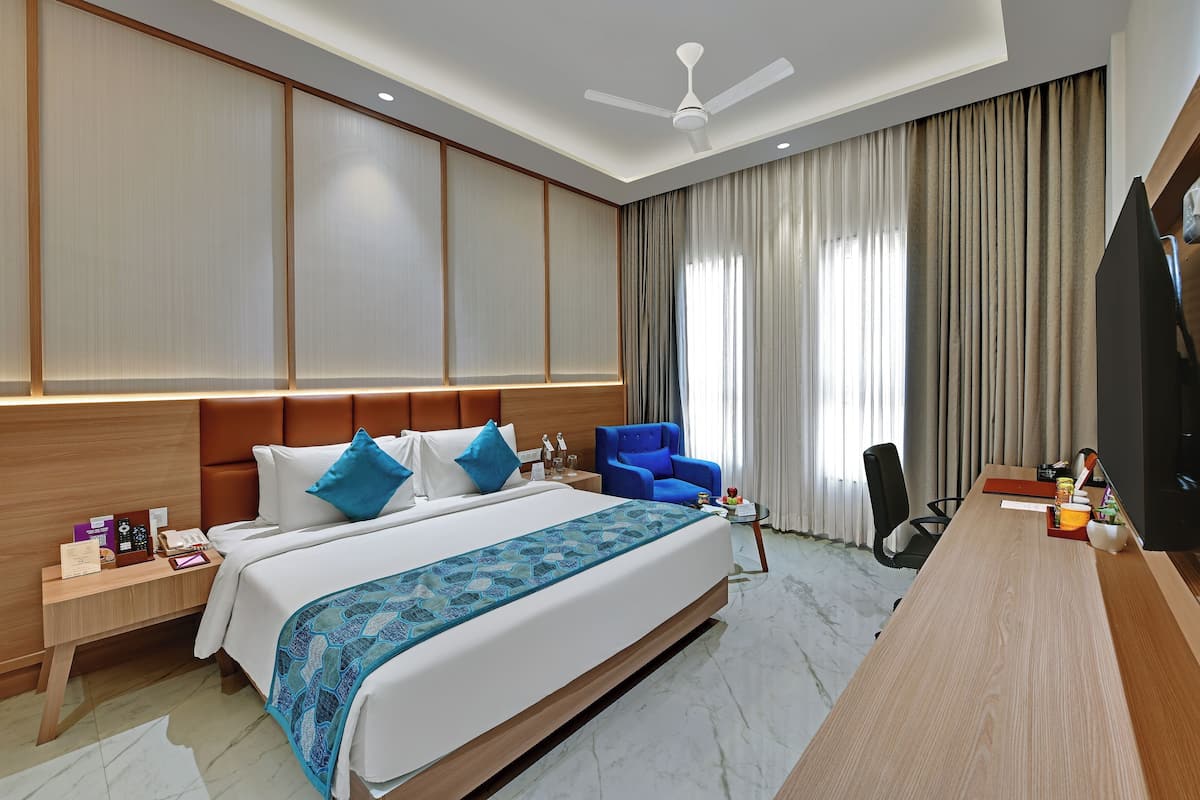 Quarto de hotel com uma cama grande, uma escrivaninha, uma cadeira, uma televisão e um ventilador de teto.