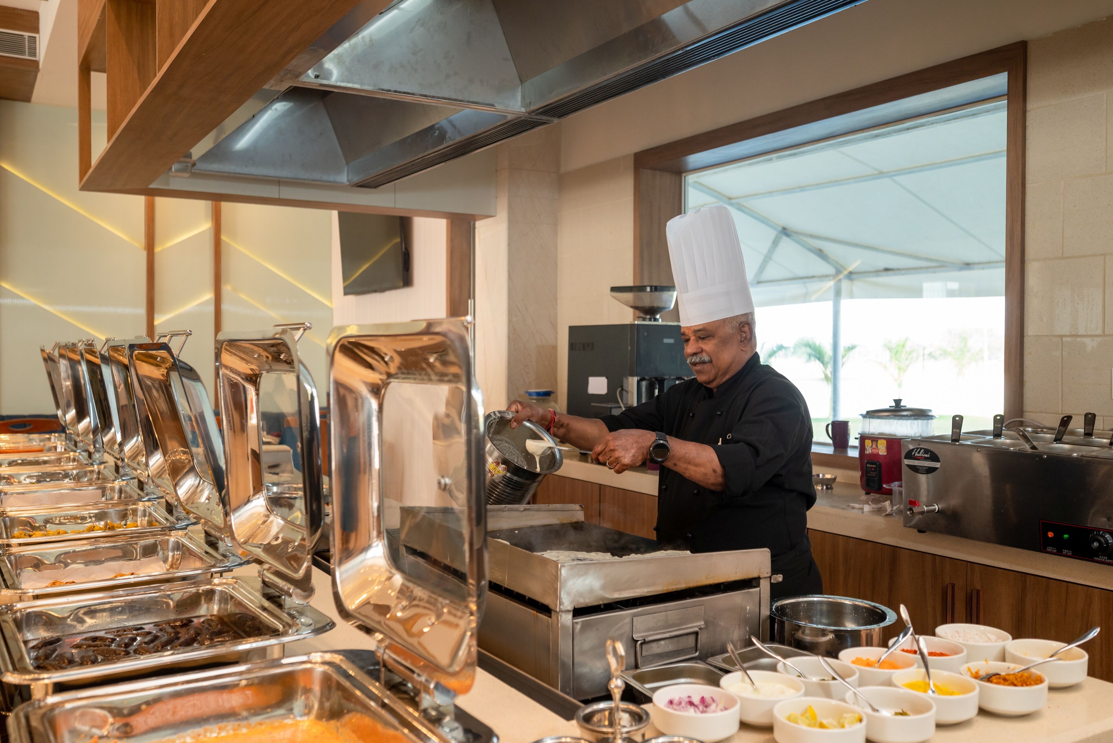 A buffet setup with various food containers and a chef preparing food.