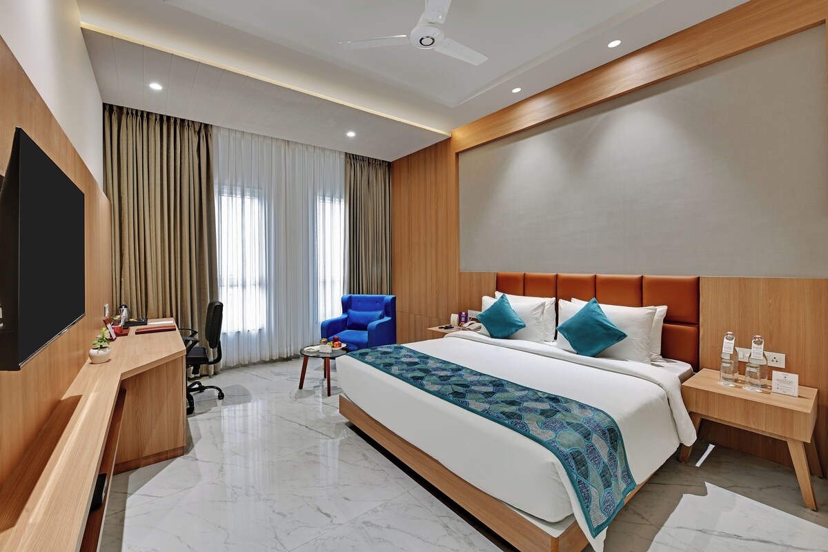 A hotel room with a bed, a desk, a chair, a TV, a ceiling fan, and a nightstand.