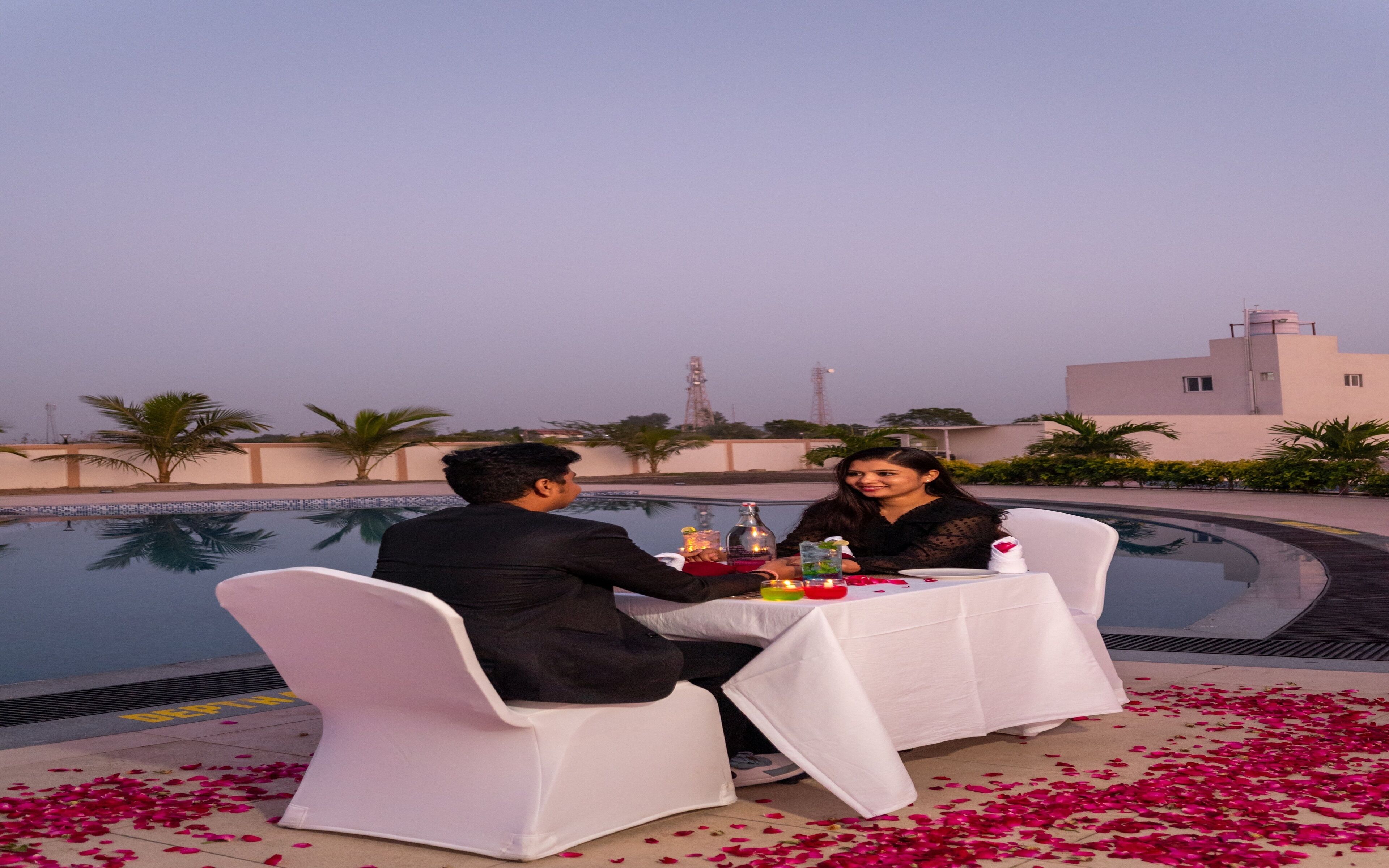A couple dining at an outdoor table by a pool, with a clear view of the surrounding architecture and palm trees.