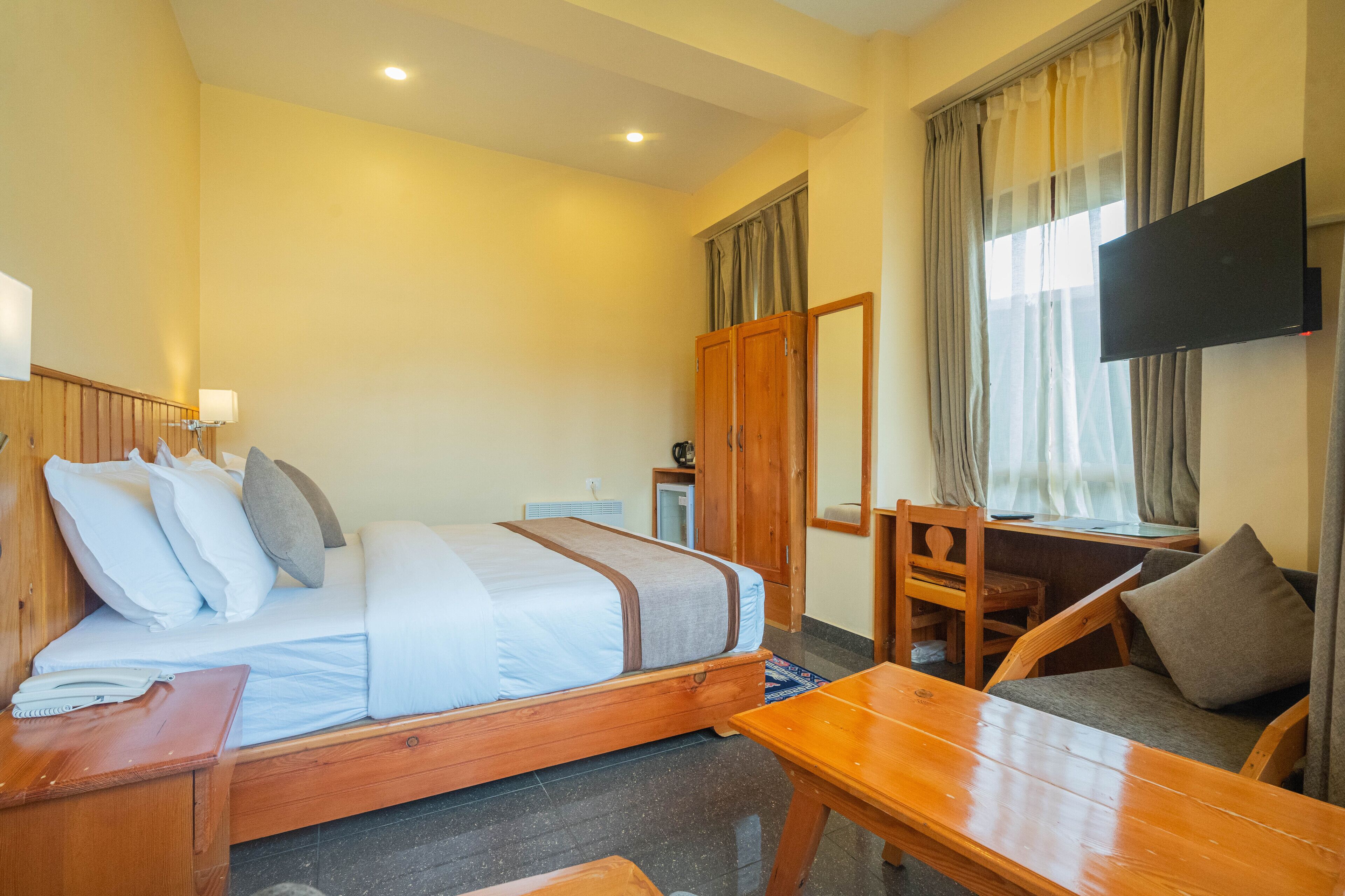 Una habitación de hotel con cama, escritorio, silla, televisión y ventana con cortinas.