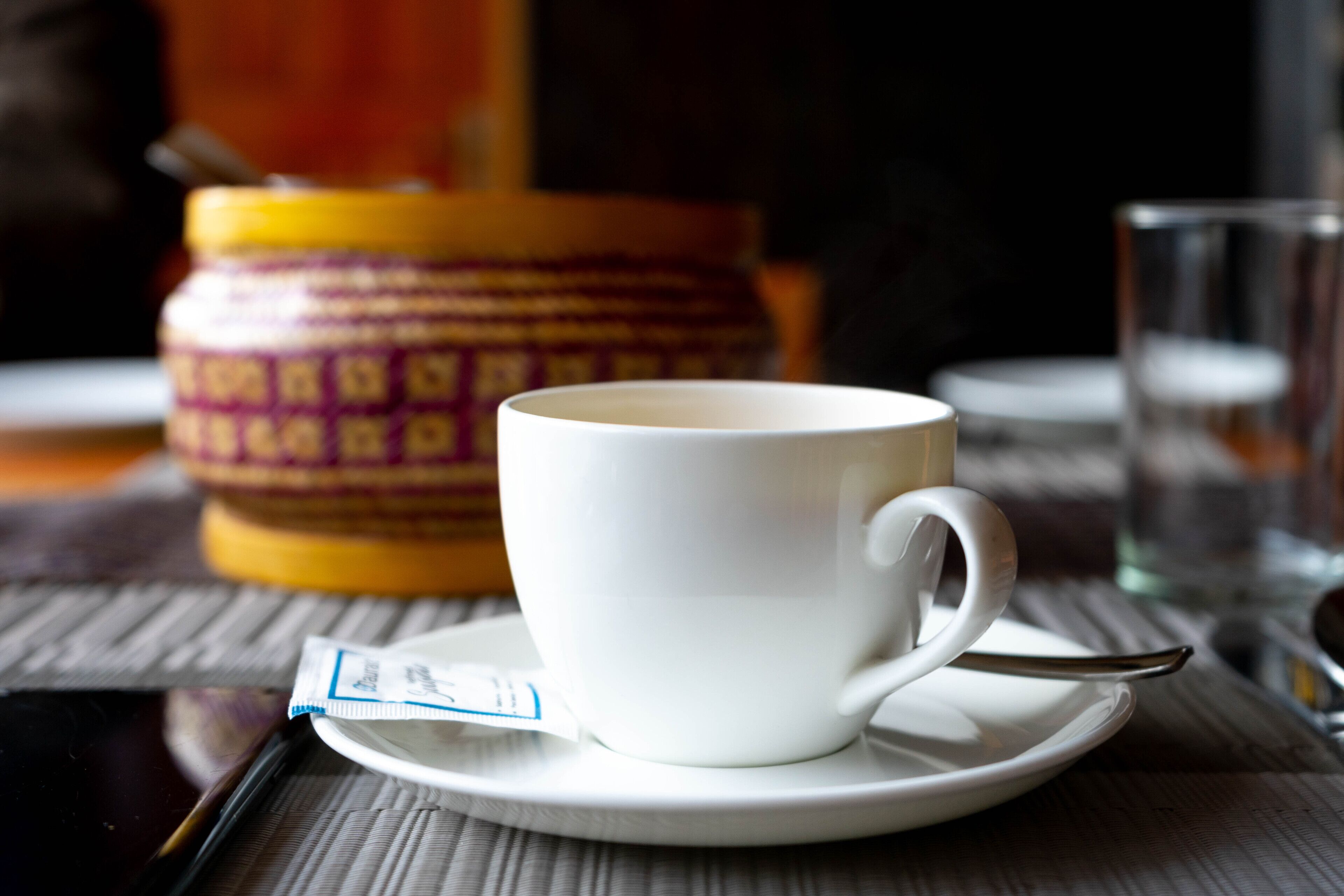 A white cup on a saucer with a spoon, a packet of tea, and a glass of water on a table.