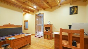 A wooden-floored room with a sofa, a desk, and a chair. A massage room door is visible in the background. - Hotel Gakyidiana (Paro)