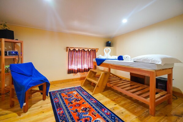 A room with a bunk bed, a chair, a small table, a shelf, and a window with curtains.