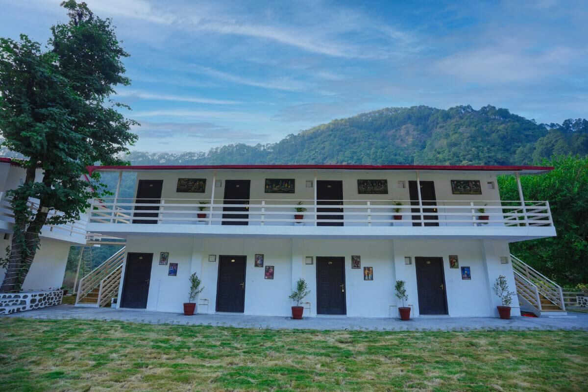 Un edificio de dos pisos con fachada blanca y tejado rojo, que cuenta con varias puertas y ventanas, rodeado de césped y árboles.