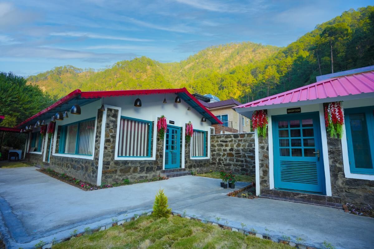A stone building with a red roof and blue shutters, a reception area with a blue door, and a mountainous backdrop.