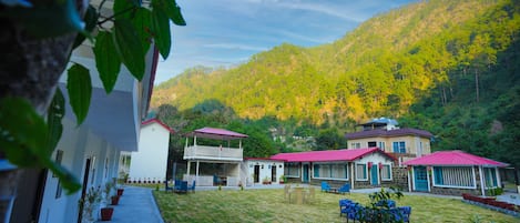 A row of white buildings with red roofs, a grassy courtyard, and a mountainous backdrop.