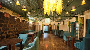 Ein Restaurant mit einer Steinwand, grünen Polstersesseln und hängenden floralen Dekorationen.