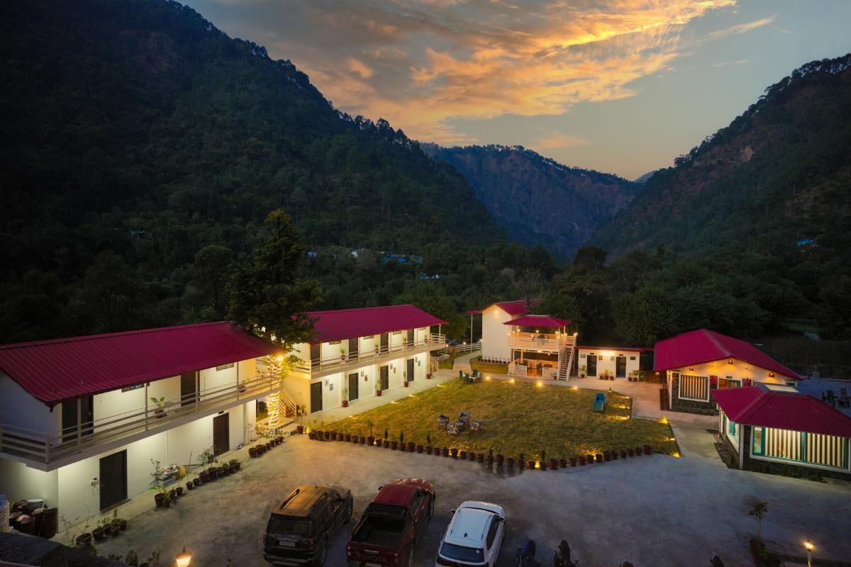 A hotel with multiple buildings, each with a red roof, situated in a valley surrounded by mountains.