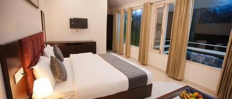 A hotel room with a bed, bedside table with a lamp, a TV mounted on the wall, and a balcony with curtains.