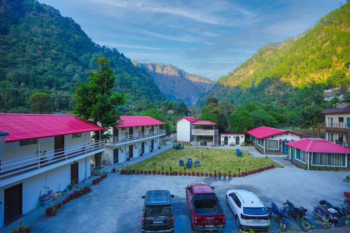 A hotel with multiple buildings, a parking area with cars and motorcycles, and a mountainous backdrop.