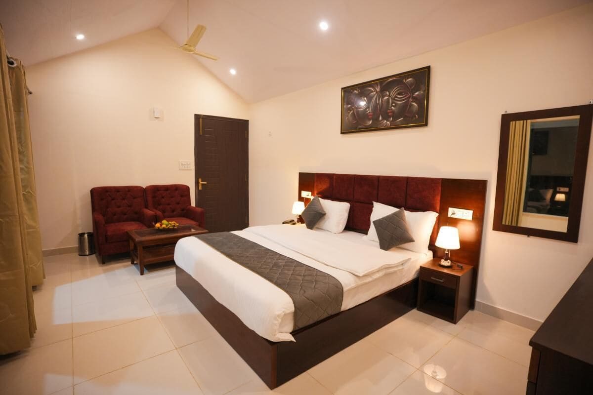 Habitación de hotel con una cama grande, dos mesitas de noche con lámparas, un sofá rojo, un ventilador de techo y una obra de arte enmarcada en la pared.
