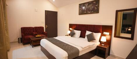 Habitación de hotel con una cama grande, dos mesitas de noche con lámparas, un sofá rojo, un ventilador de techo y una obra de arte enmarcada en la pared.