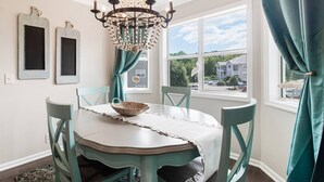 Un comedor con una mesa redonda, sillas color turquesa, una araña y vistas a una casa a través de una ventana.