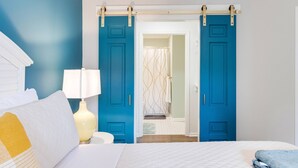 Un dormitorio con una cama, una mesita de noche, una lámpara y una puerta corrediza azul que da al baño.