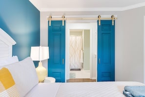 Une chambre à coucher comprenant un lit, une table de chevet, une lampe et une porte coulissante bleue donnant sur une salle de bain.