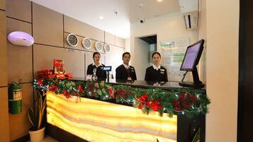 A hotel reception desk with three staff members, a digital screen, and holiday decorations.