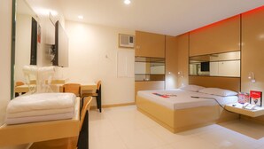 A modern hotel room with a bed, a desk, a chair, a mirror, and a bedside table with a lamp. - Hotel Sogo General Trias (General Trias)