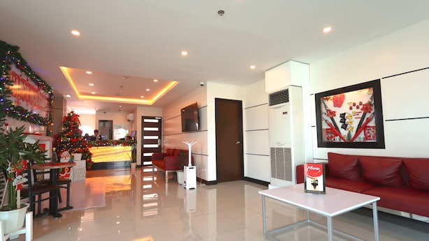 A modern hotel lobby with a Christmas tree, a reception desk, a red sofa, and a framed artwork on the wall. - Hotel Sogo General Trias (General Trias)