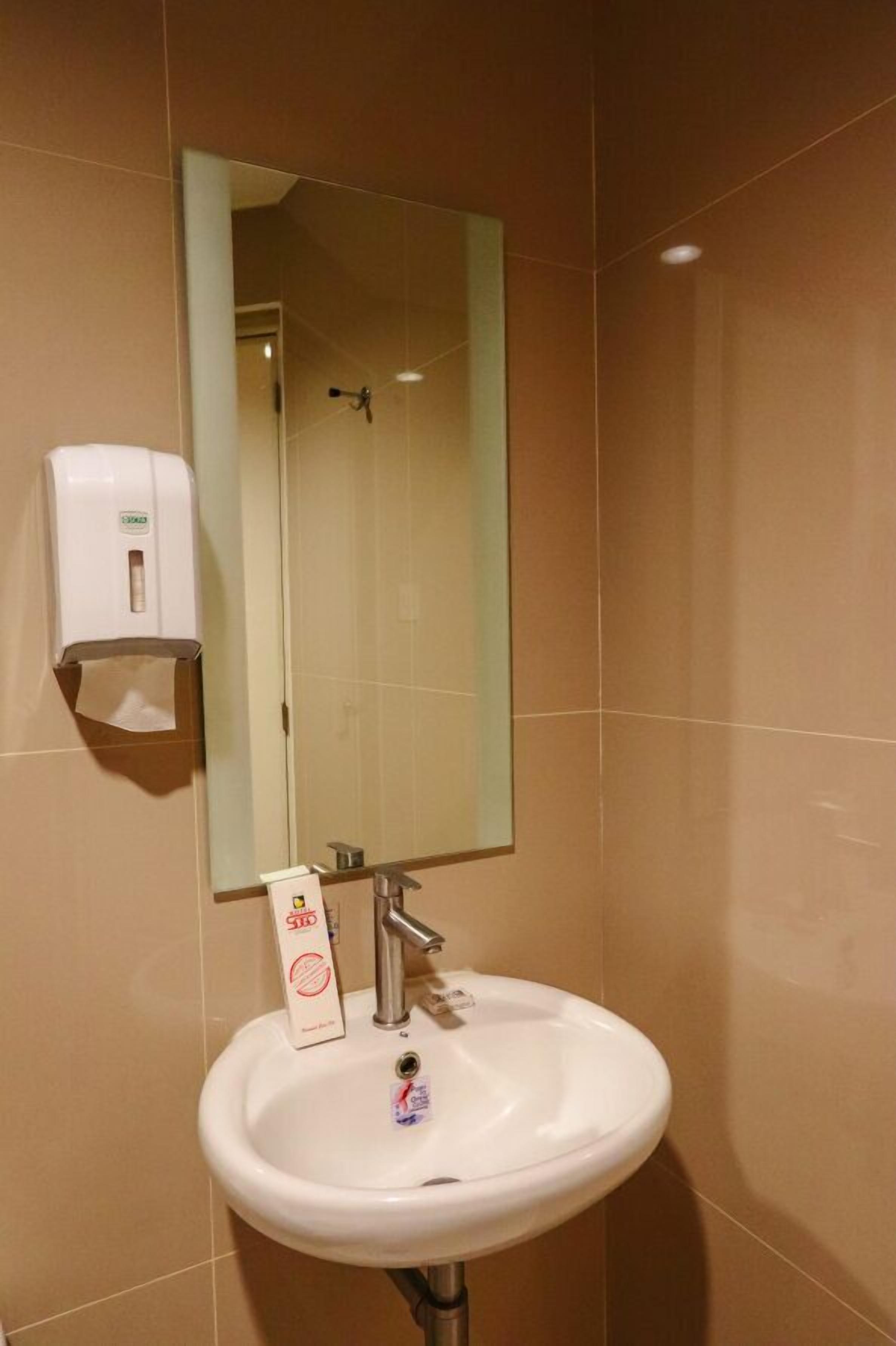 A bathroom with a white sink, a mirror, and a soap dispenser.