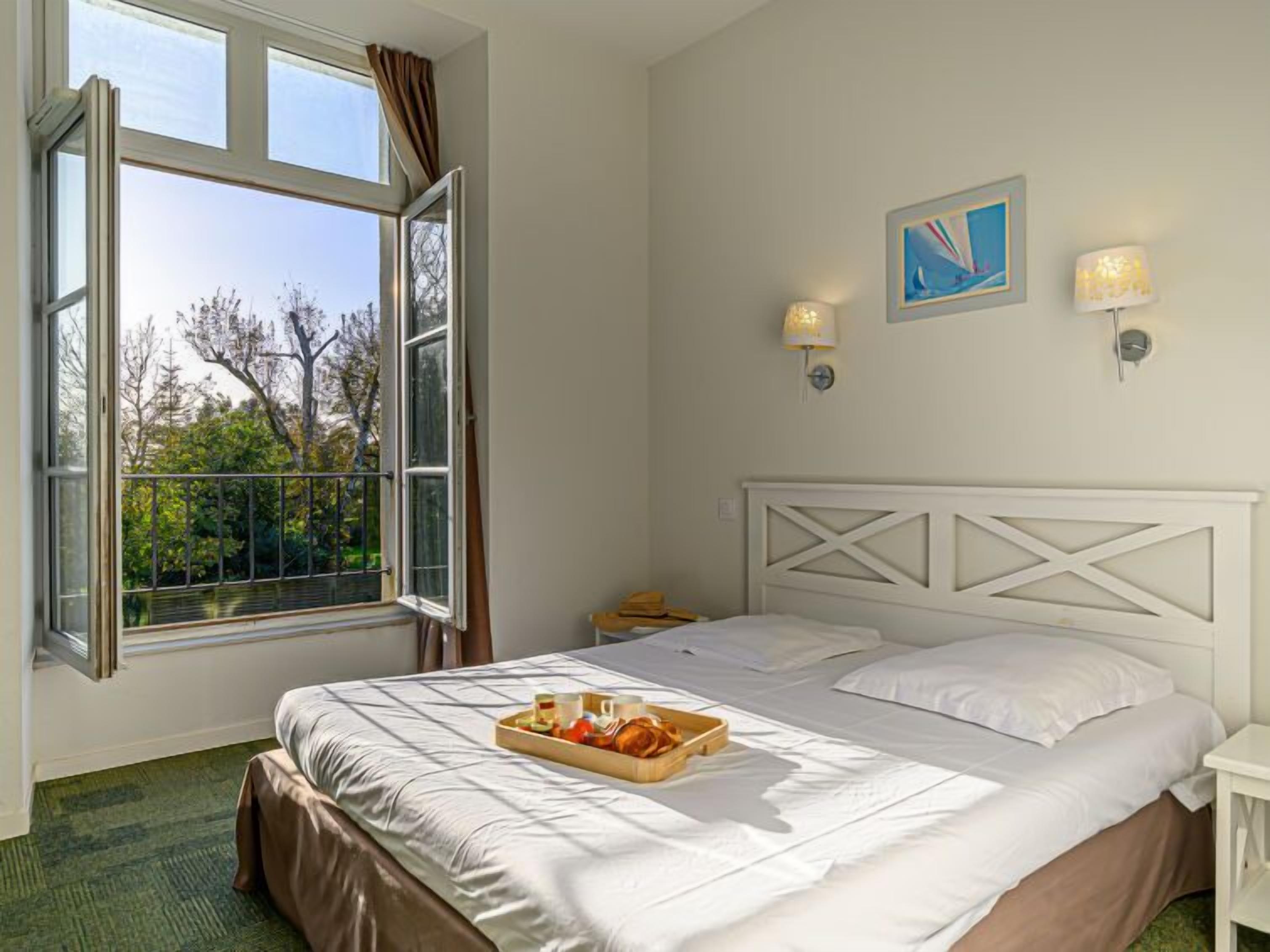 Habitación de hotel con cama, ventana con cortinas, bandeja de desayuno y dos lámparas fijadas a la pared.