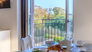 Mesa con platos, tazas y tetera, con vistas a un balcón y árboles.