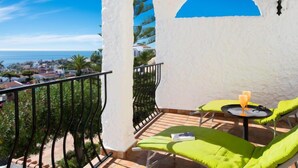 Ein Balkon mit Meerblick, grüne Sitzgelegenheiten und ein Tisch mit einem Getränk.