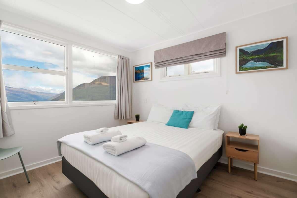 Ein Schlafzimmer mit einem großen Bett, zwei Nachttischen, einem Fenster mit Vorhängen und Blick auf Berge.