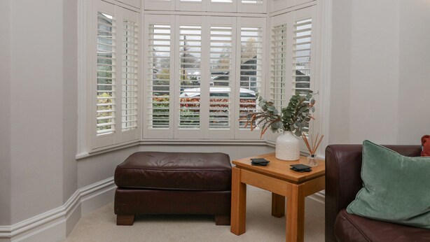 A corner room with a bay window, a leather bench, a wooden table, and a green cushion.
