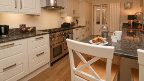 A modern kitchen with white cabinetry, a stainless steel range hood, a granite countertop, and a white chair.